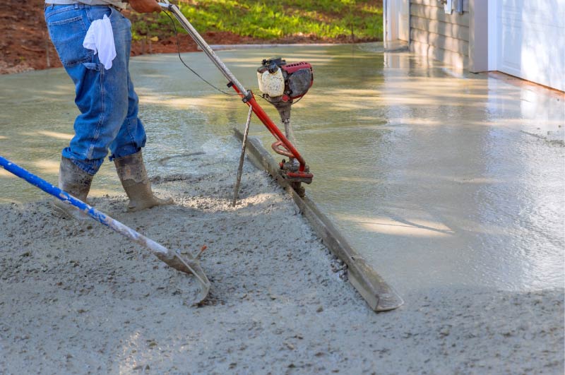 Contractor finishing a freshly poured concrete driveway with a bull float<br />

