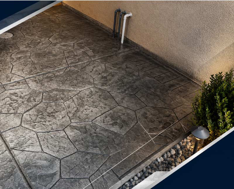 Stamped concrete walkway with irregular flagstone pattern beside landscaped garden bed