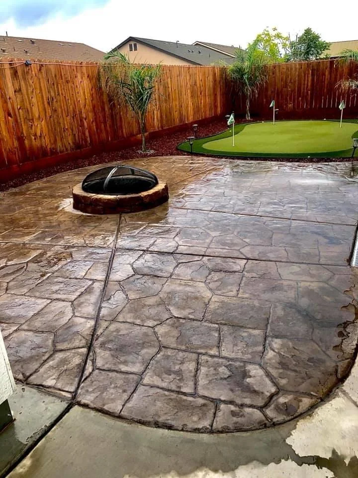 concrete stamp A landscaped backyard featuring a grassy area, stone walkway, and wooden benches surrounded by lush greenery and palm trees.
